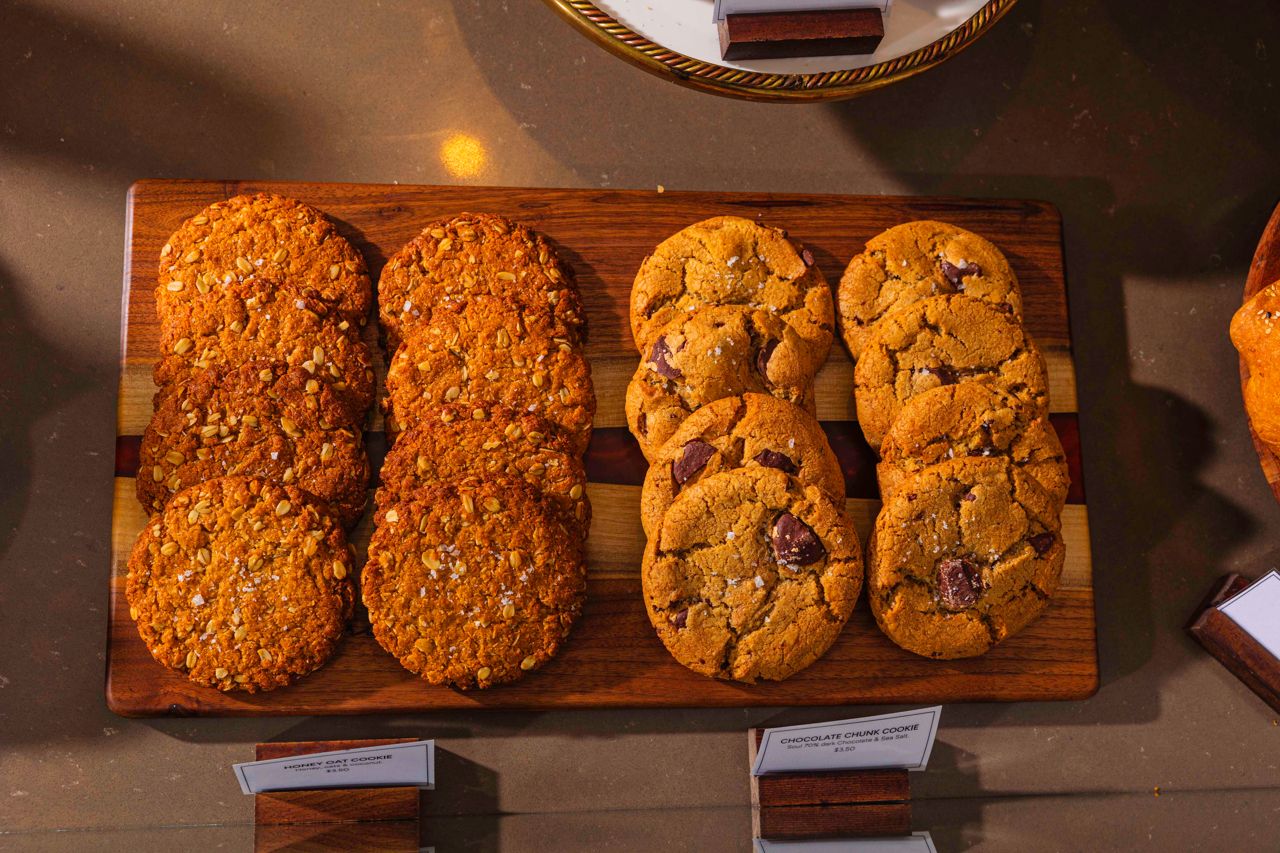 A wooden cutting board displays honey-oat and chocolate chunk cookies