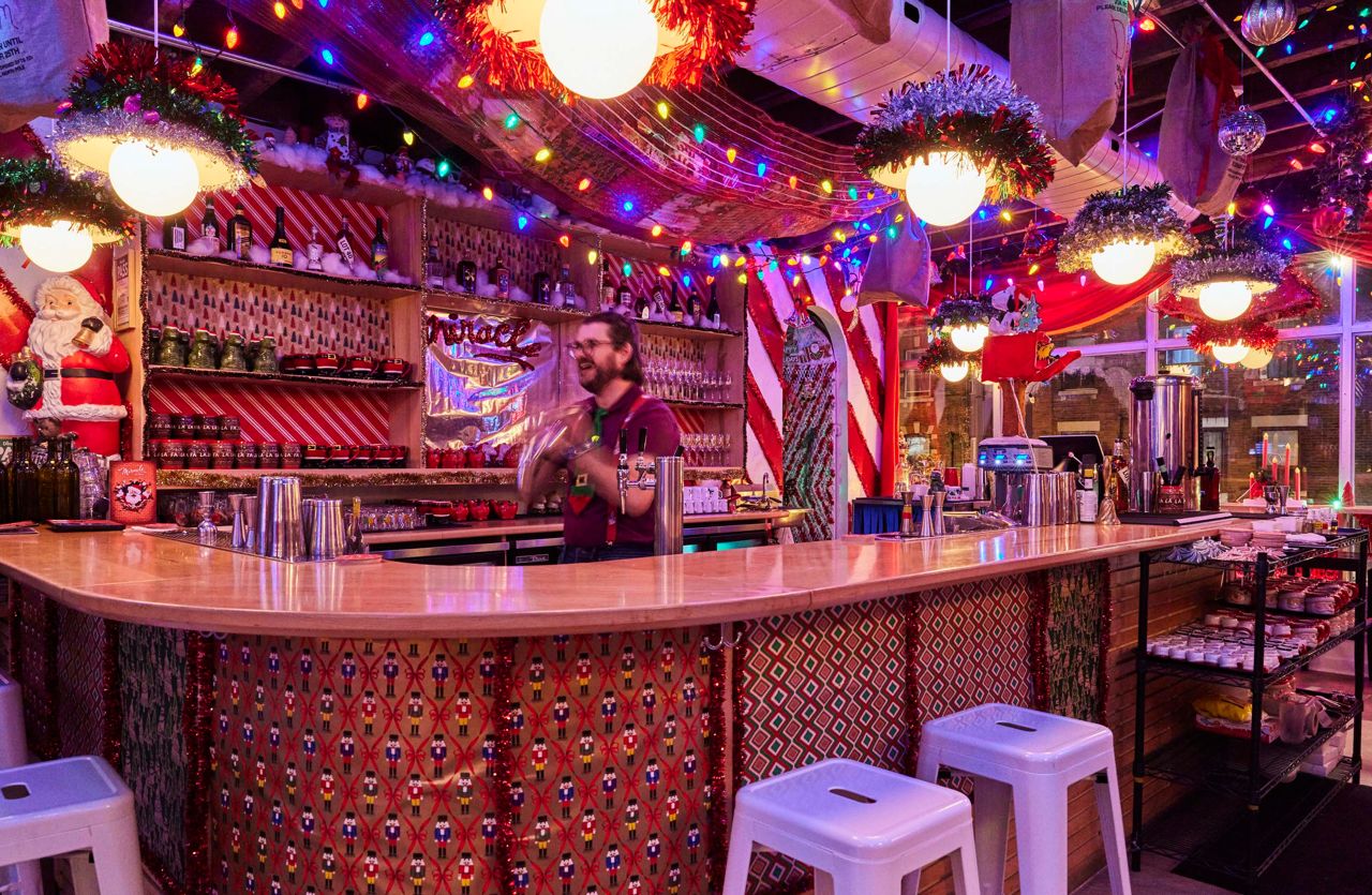 A bartender shakes a cocktail behind a bar decorated for Christmas