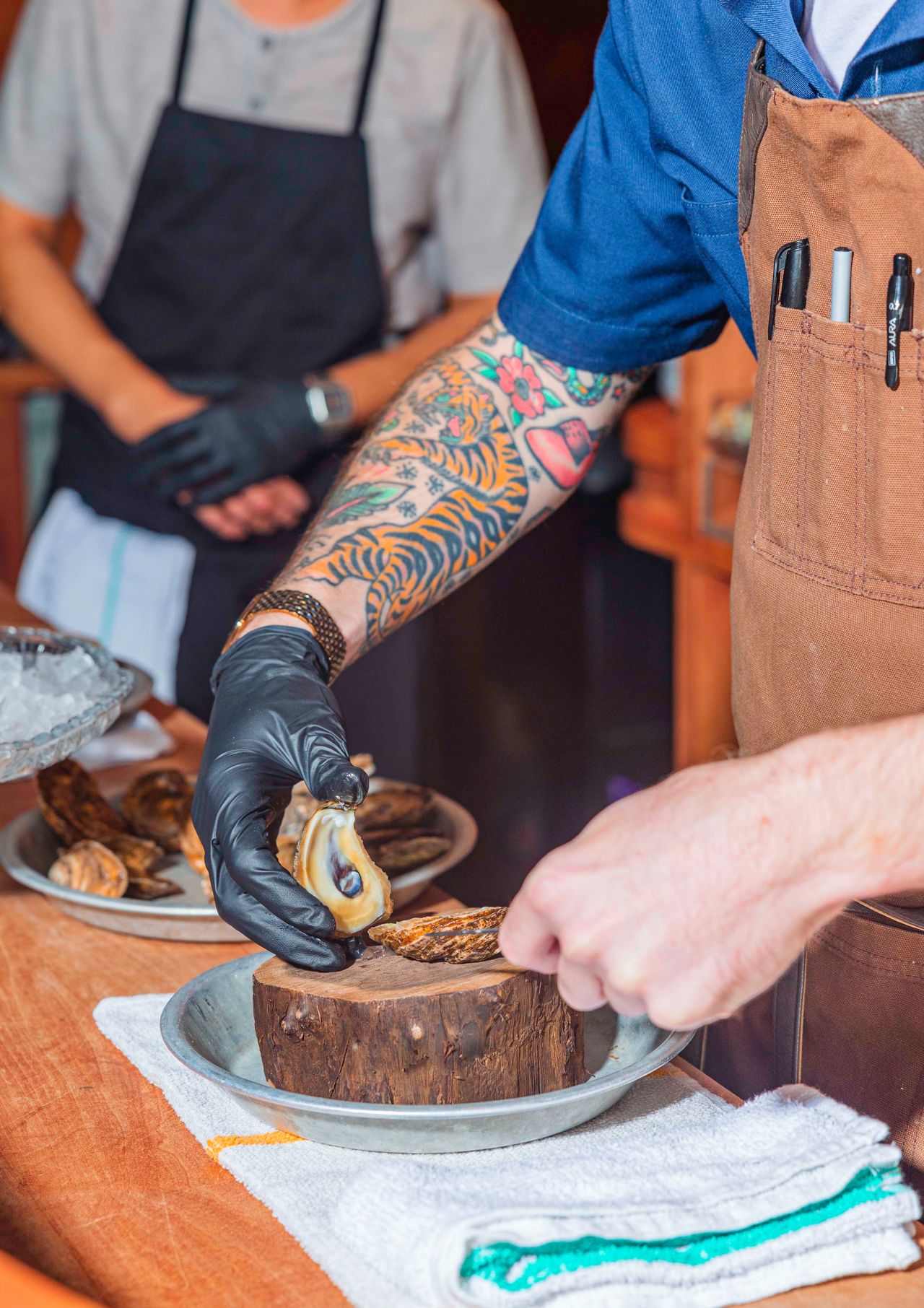 A person with tattoos on their arm shucks an oyster